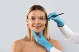 Woman smiling while plastic surgeon holds marker to face to indicate surgical site during facelift consultation.