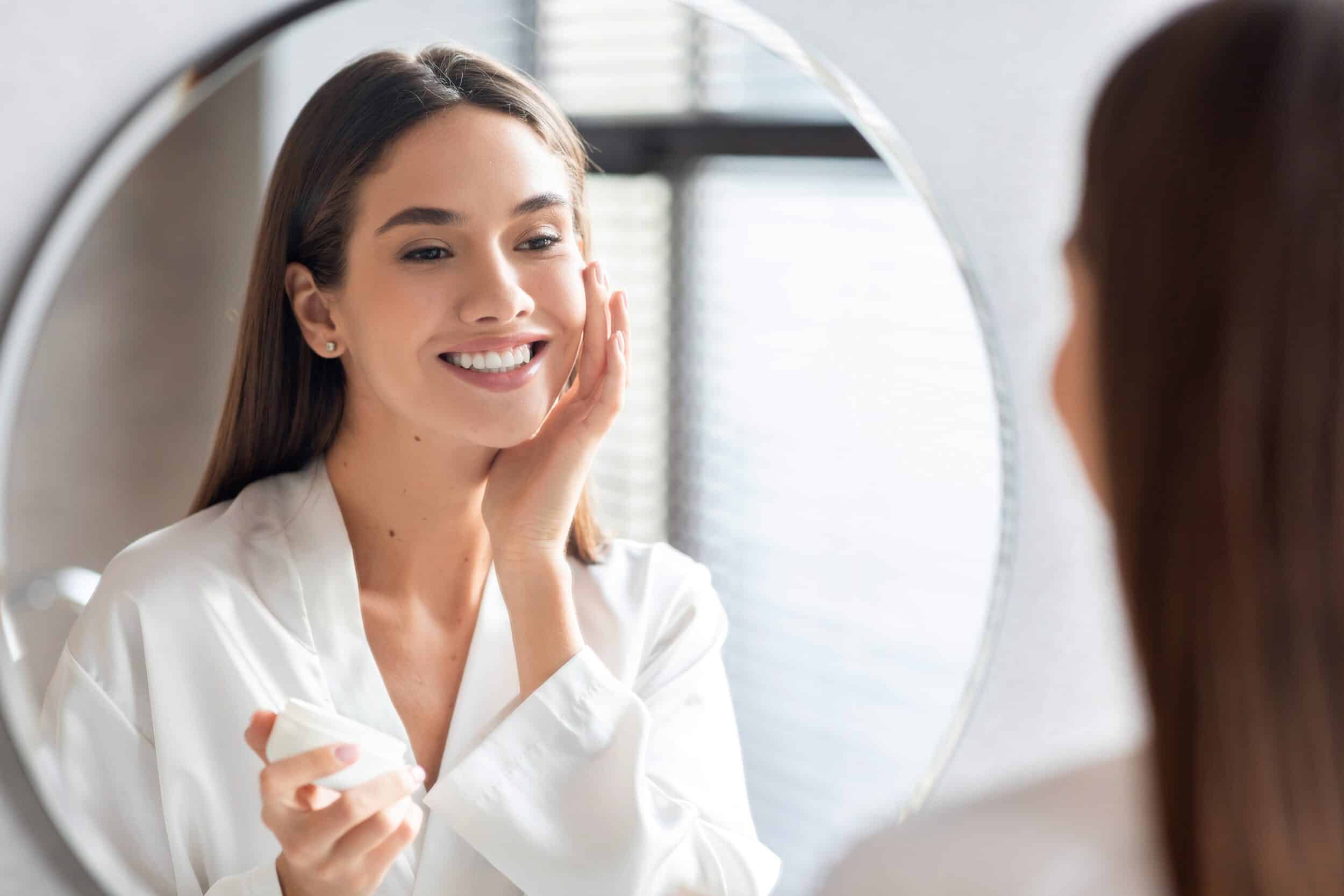 Woman smiling while looking at herself in the mirror after Virtue RF Microneedling
