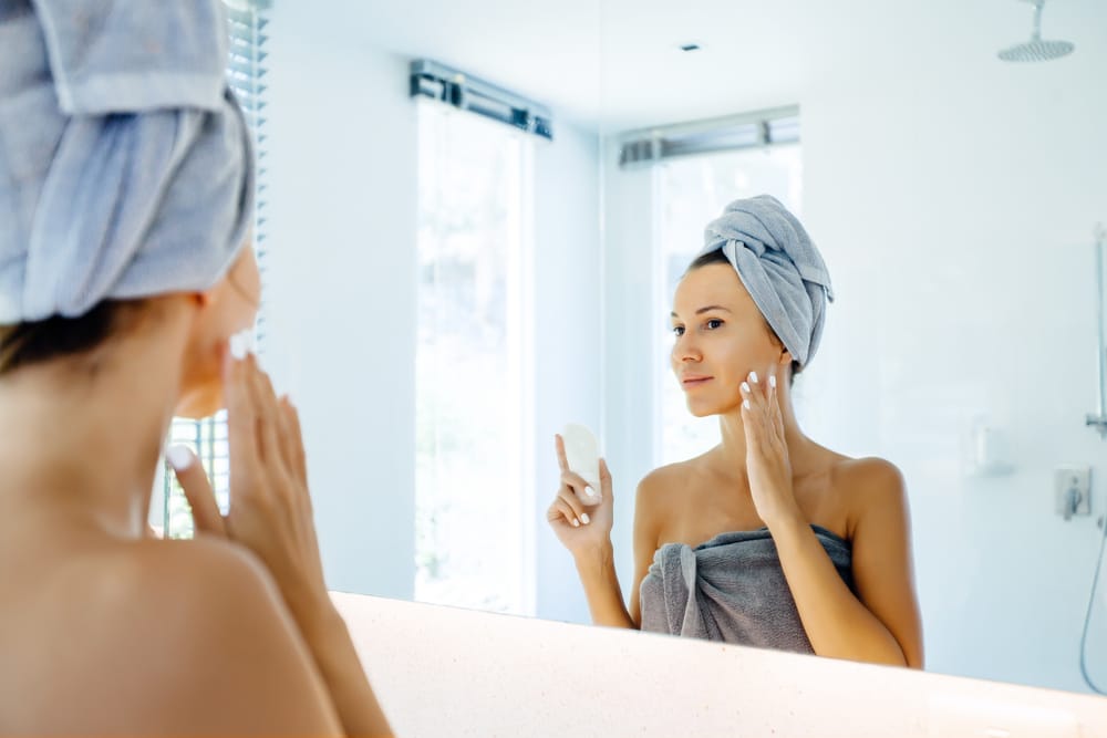 Woman looking in the mirror at her clear skin from Motus AZ+ laser treatment in Dallas, TX